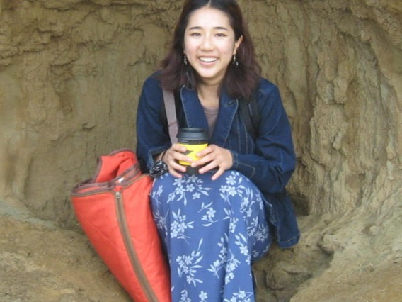A woman in a blue flowered skirt with a coffee cup sitting in a natural cave