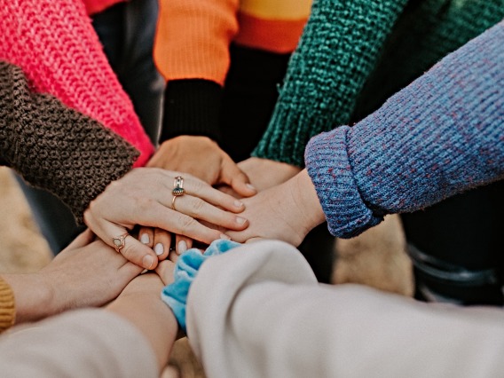A group of people with different colored sleeves touching hands.