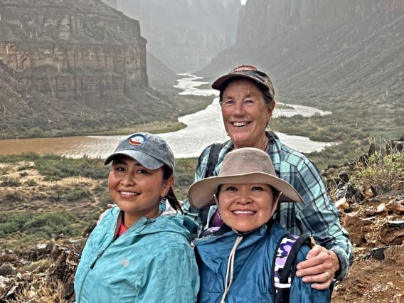 Three women stand together in the Grand Canyon with the Colorado River behind them.