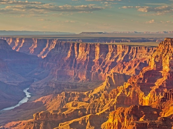 The Grand Canyon and Colorado River under a blue sky at sunset.