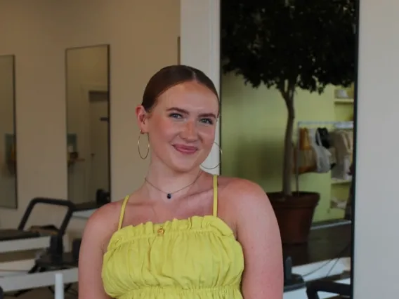 Audrey Lockman: photo of woman in a yellow top, brown hair pulled back, and hoop earrings smiling at camera