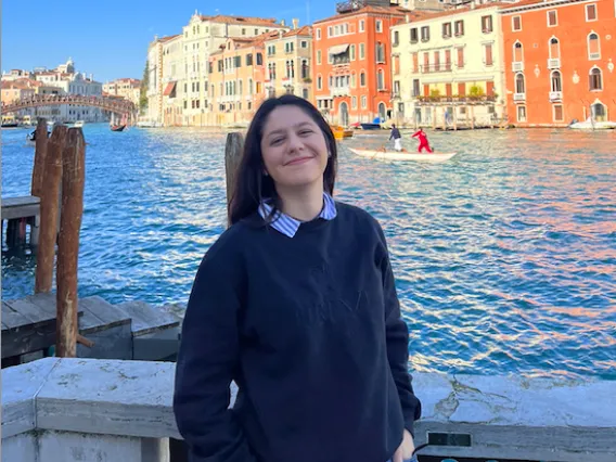 Alyssa Paredes: Brown haired woman standing and smiling in front of buildings and a body of water