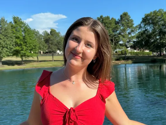 Hope Barton: woman with brown hair wearing a red dress smiling in front of a body of water