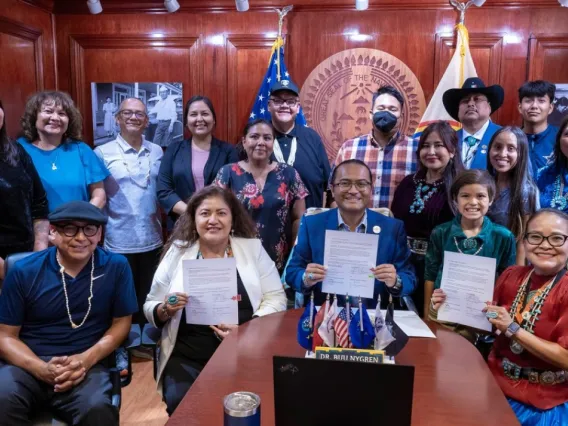 A group of people smile around a table, holding up documents.