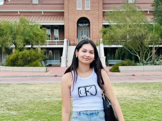 Nandika Barjatya: Woman with long dark hair standing in front of the Old Main building at U of A. Se is wearing a grey tank top and blue jeans. 