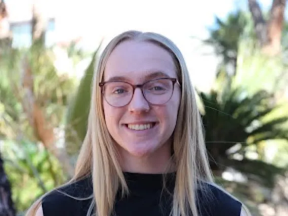 Grace Toftner: Blonde woman with round, brown glasses wearing a black shirt smiling at the camera