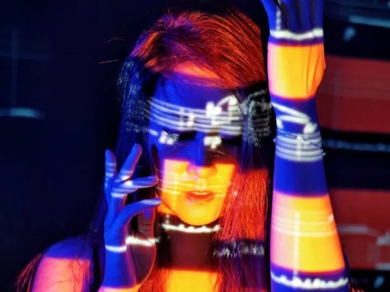 Kay He, woman with long hair posed with both arms pointed upward with music notes, yellow, and blue light projected on her.