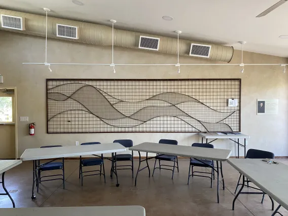 Watershed Management Group Living Lab, two tables and chairs in a room with a metal art piece on the wall in the background with curved lines representing water 