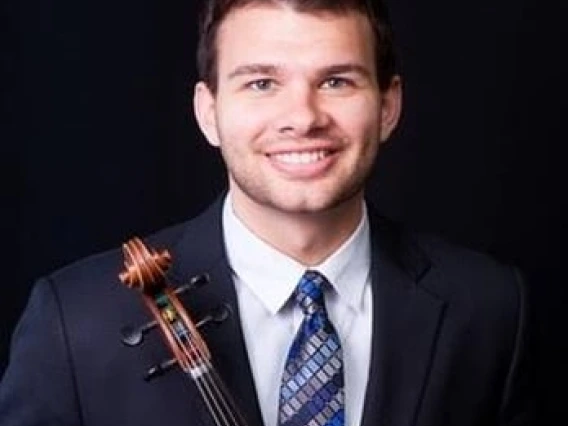 Headshot of Ivan Ugorich in front of a black background holding a violin.