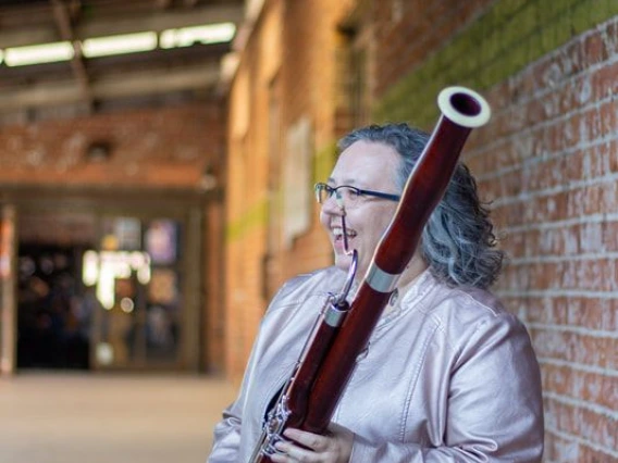 Cassandra Bendickson holding a bassoon in front of a brick wall.