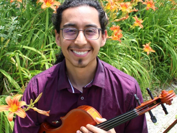 Headshot of Esteban Hernandez Parra holding a viola in front of orange flowers.