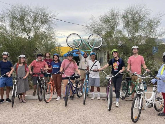 A group of people with bicycles stand outdoors smiling.