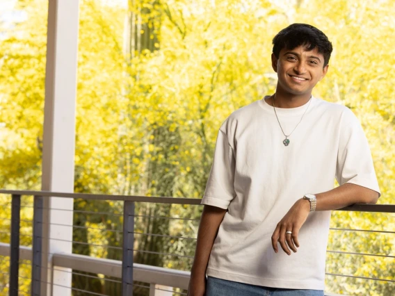 Ojas Sanghi leans against a railing with a tree behind him.