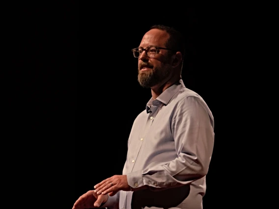 Ladd Keith stands before a dark background while giving a speech.