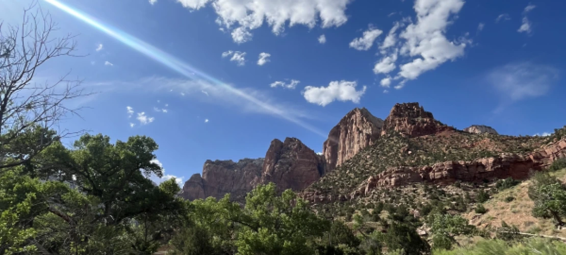Small clouds in a beautiful blue sky over. a trail path in Zion National Park.