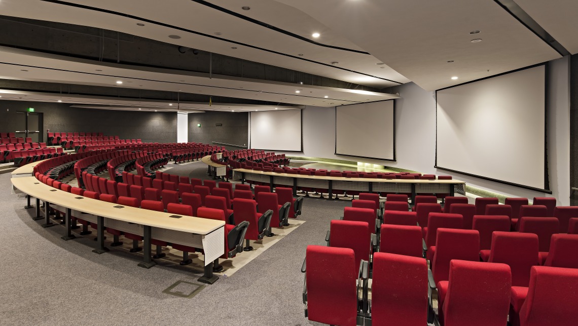 Photo of room N102 in the ENR2 building on the University of Arizona campus. Red seating and tables semi-circling a lecture stage.