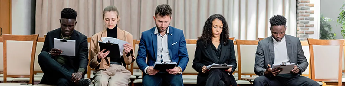 Five people sitting side-by-side each looking at papers on clipboards.