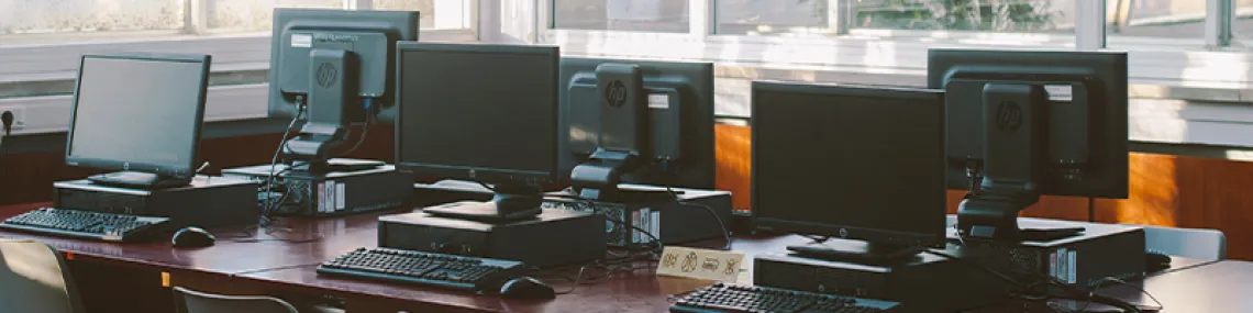 several desktop computers on wooden table with light coming through the windows.