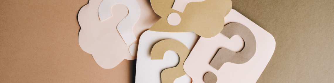 A stack of question marks made out of neutral-toned brown, white, and pink construction paper. 