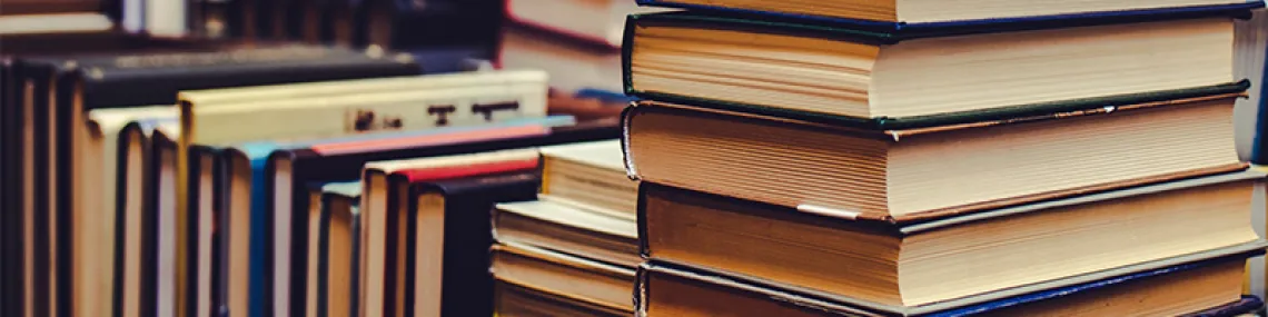 to the left are books laying side down in a row. to the right is a stack of books. their covers are missing and their bind colors are muted.