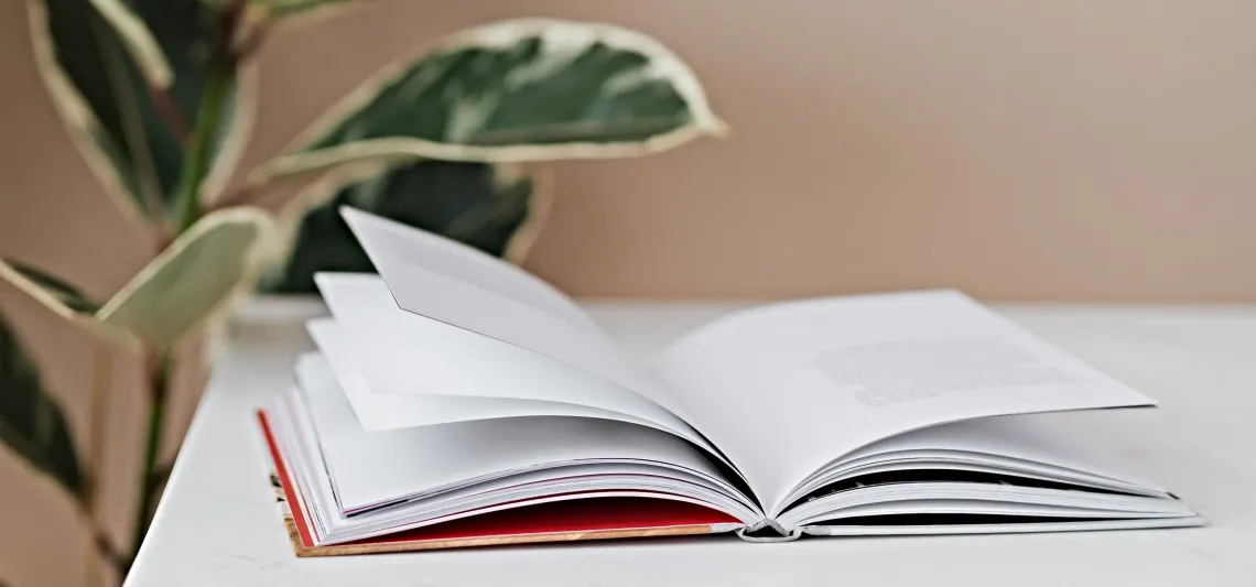 An open book on a table next to a plant.