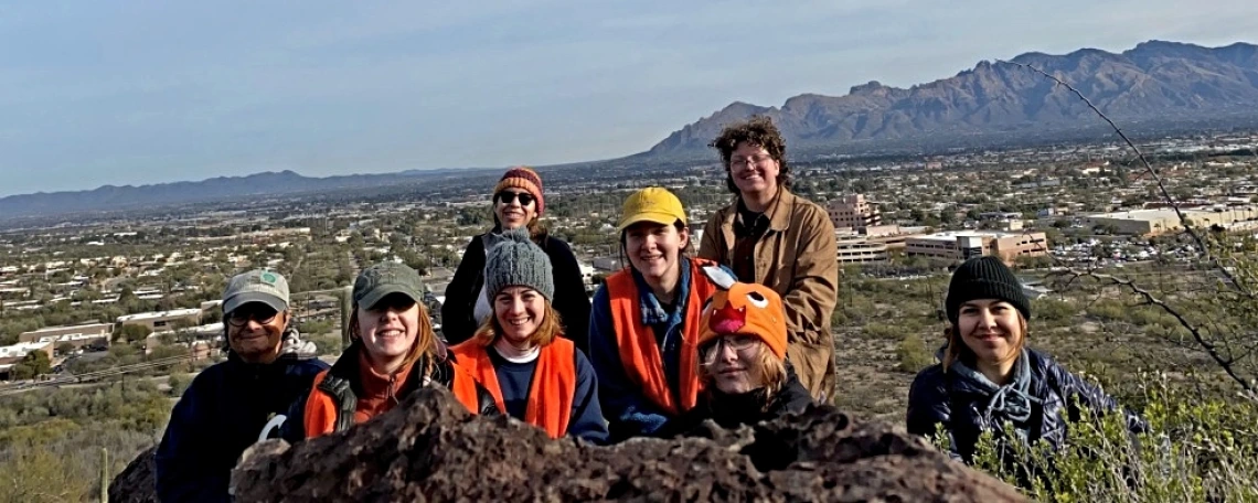 Students pose smiling outdoors with mountains in the background.