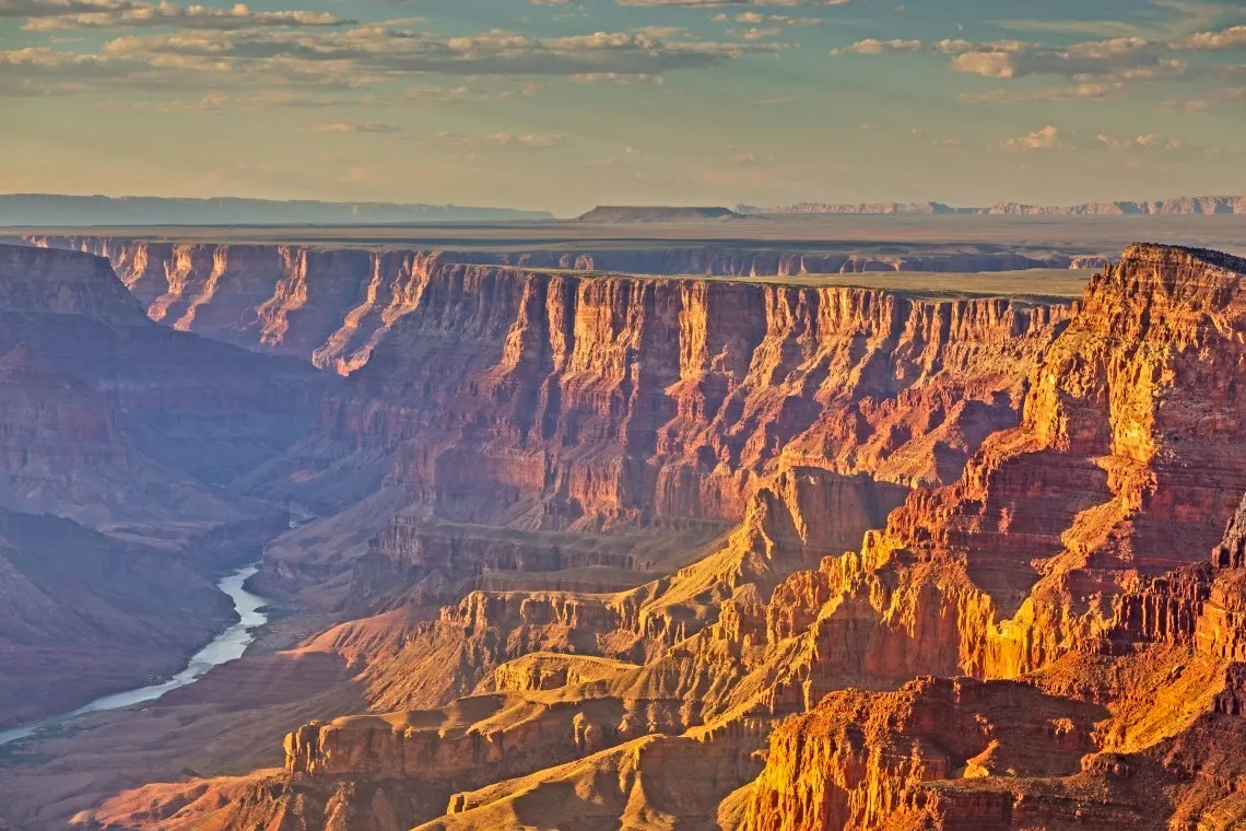 The Grand Canyon and Colorado River under a blue sky at sunset.