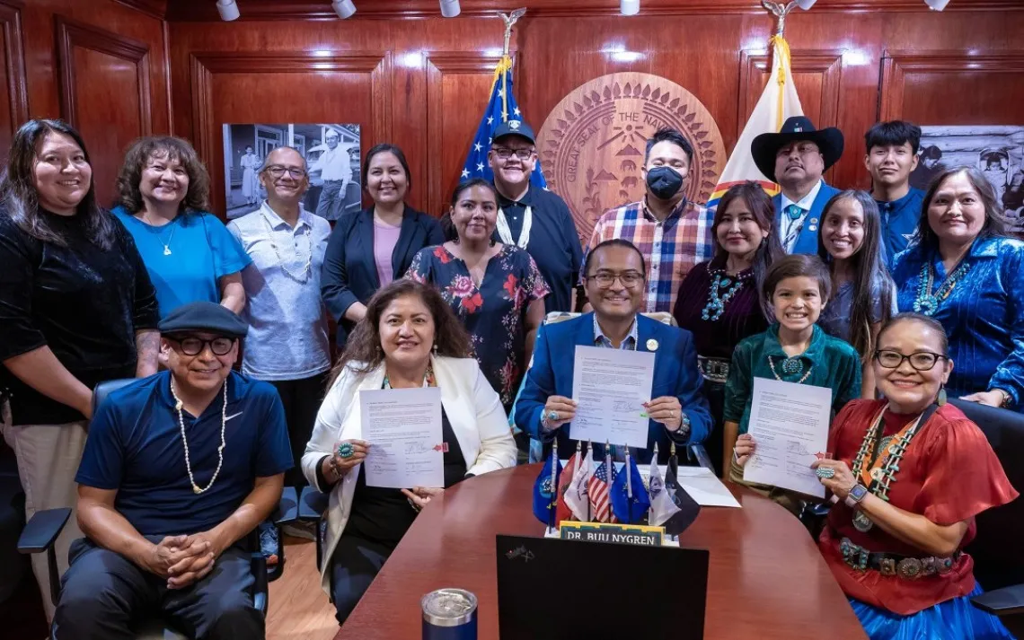 A group of people smile around a table, holding up documents.