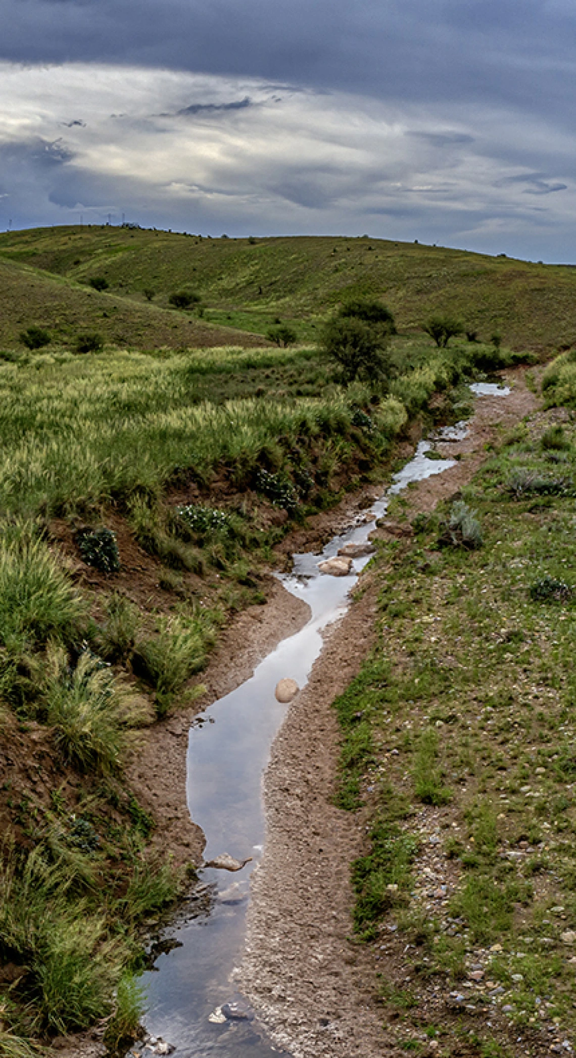 Small stream running between grassy patches and hills, dark grey sky