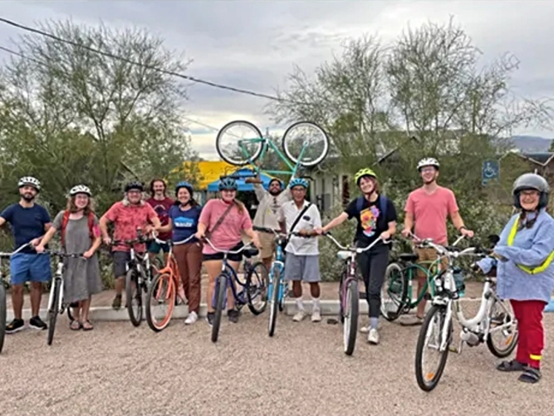 People stand together outside smiling and holding bicycles.