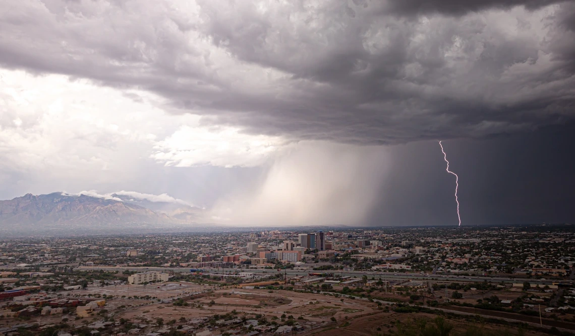 A raincloud brings rain and lightning over the desert landscape.