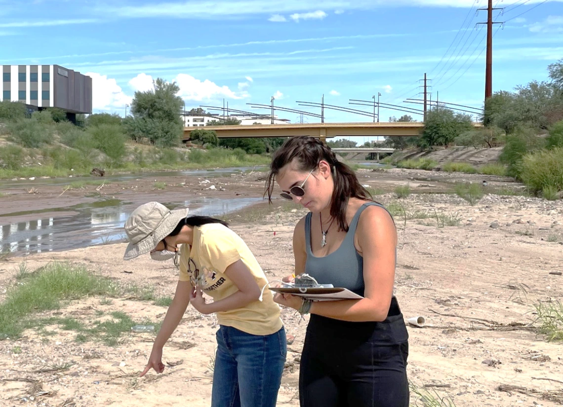 Two student researchers examining the ground in a desert wash