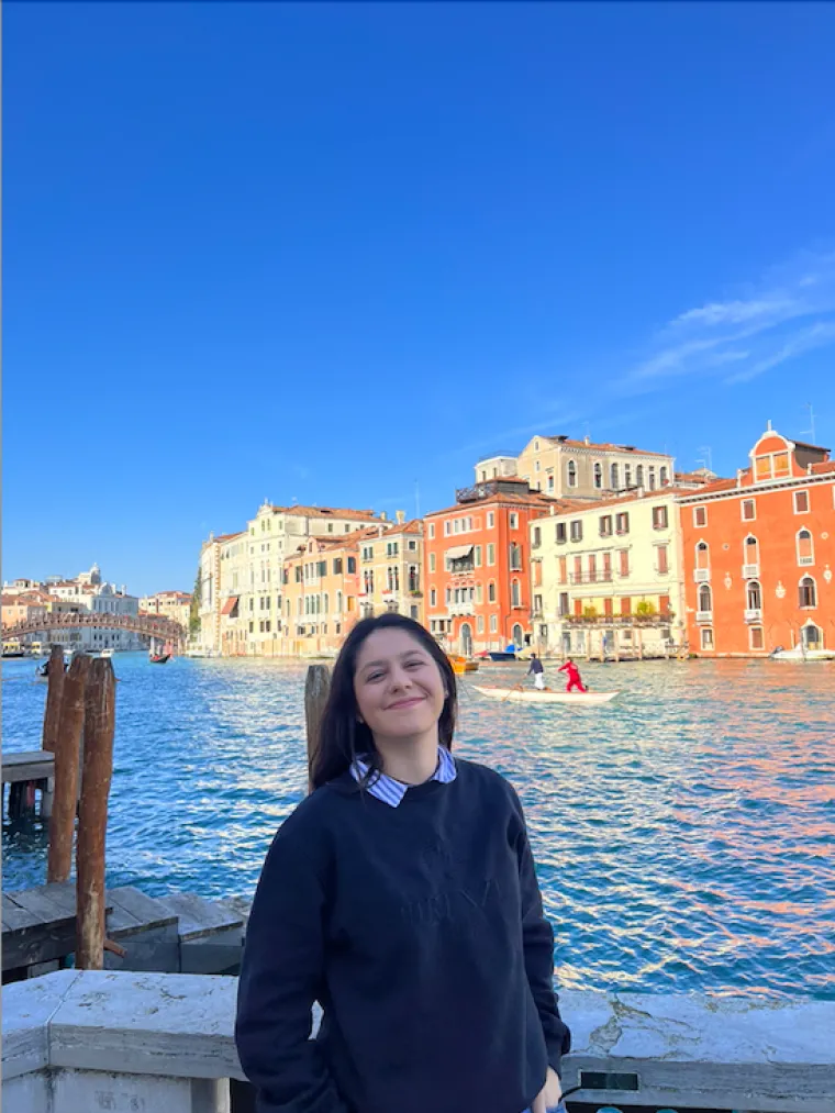 Alyssa Paredes: Brown haired woman standing and smiling in front of buildings and a body of water