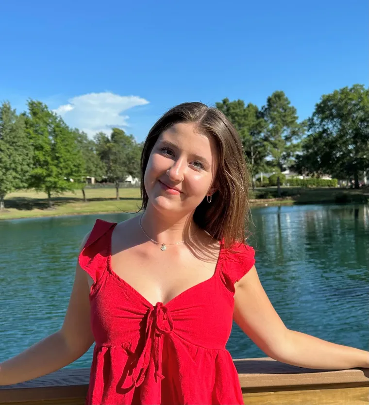 Hope Barton: woman with brown hair wearing a red dress smiling in front of a body of water