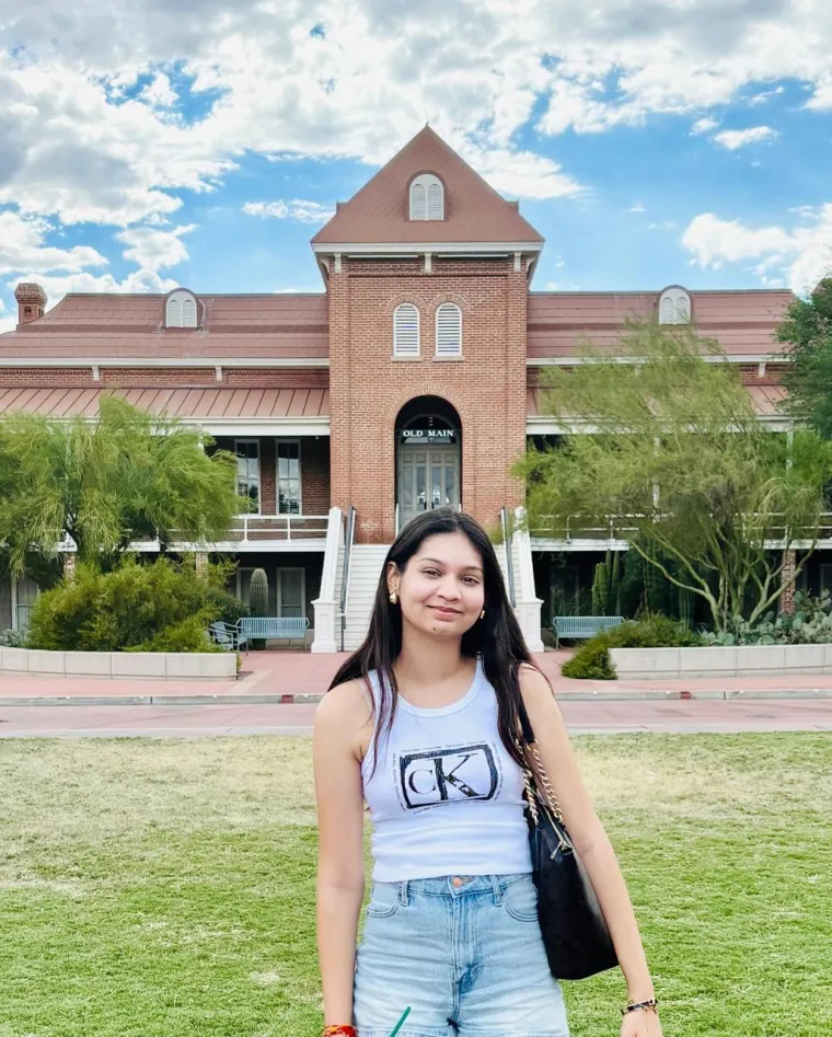 Nandika Barjatya: Woman with long dark hair standing in front of the Old Main building at U of A. Se is wearing a grey tank top and blue jeans. 