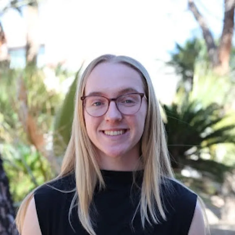 Grace Toftner: Blonde woman with round, brown glasses wearing a black shirt smiling at the camera