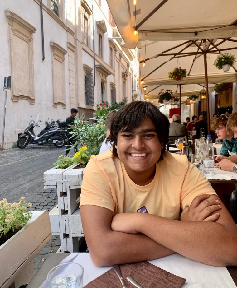 Headshot of Dev Patel sitting at an outdoor table