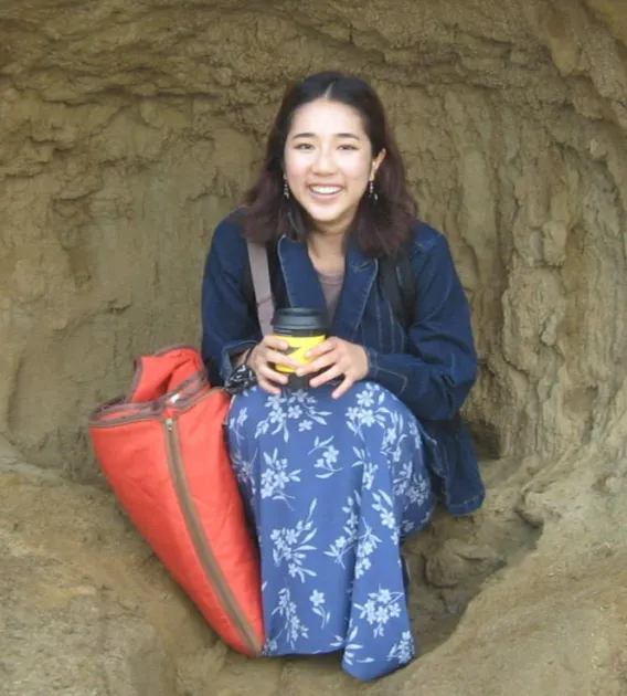 A woman in a blue flowered skirt with a coffee cup sitting in a natural cave