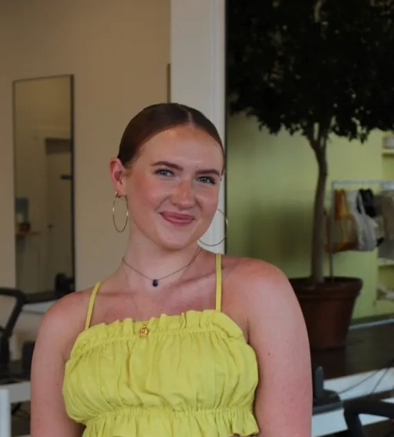 Audrey Lockman: photo of woman in a yellow top, brown hair pulled back, and hoop earrings smiling at camera