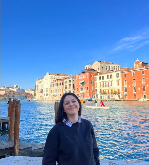 Alyssa Paredes: Brown haired woman standing and smiling in front of buildings and a body of water