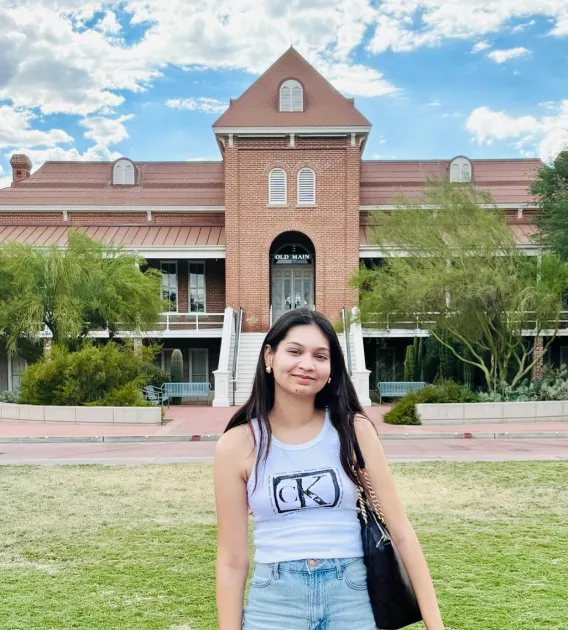 Nandika Barjatya: Woman with long dark hair standing in front of the Old Main building at U of A. Se is wearing a grey tank top and blue jeans. 