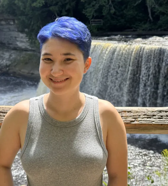 Zoe Johnson: Woman with short, blue hair standing in front of a waterfall