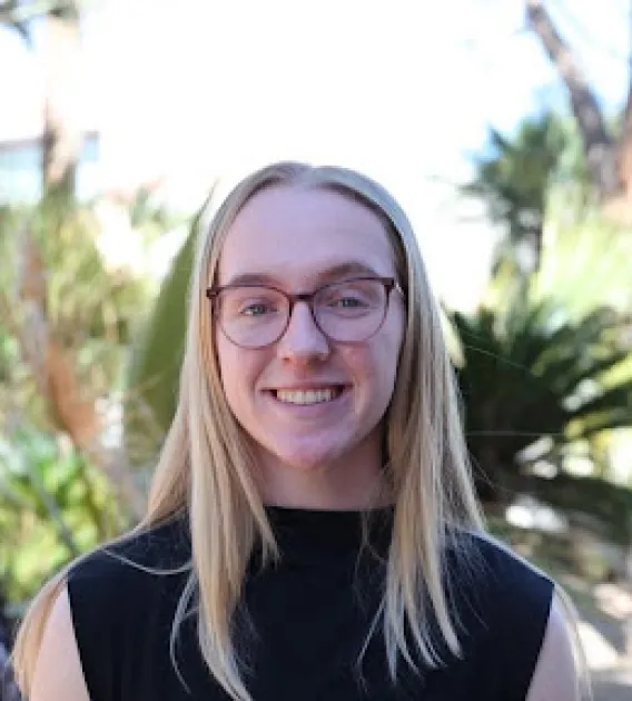 Grace Toftner: Blonde woman with round, brown glasses wearing a black shirt smiling at the camera