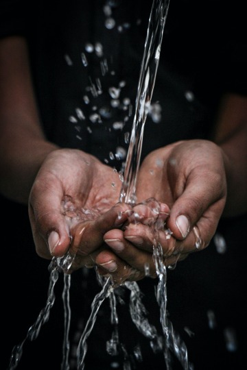 A person holds their hands together while water falls into their palms from above.