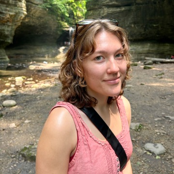 A woman in a pink tank top standing in a canyon, smiling
