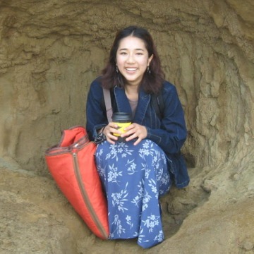 A woman in a blue flowered skirt with a coffee cup sitting in a natural cave