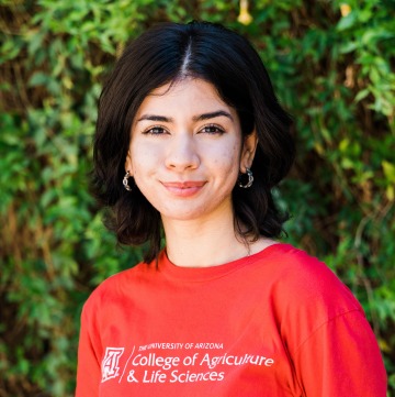 A woman smiling in front of a bush wearing a red UArizona t-shirt
