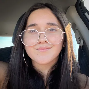 A woman sitting in a car wearing oversized white-rimmed glasses