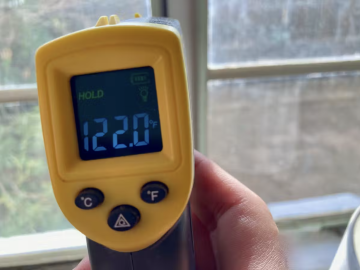 A yellow thermometer held near a window pane reads 122.0 degrees F.