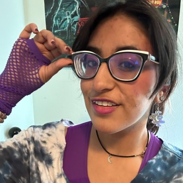 A woman with short hair adjusting her black and white rimmed glasses, wearing purple fishnet gloves